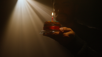 Mano sosteniendo un pastel con una vela encendida, iluminado por un haz de luz