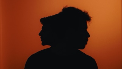 Dos siluetas de perfil superpuestas sobre un fondo naranja