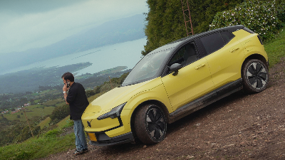 Automóvil eléctrico amarillo en un mirador de montaña, con una persona apoyada en el capó